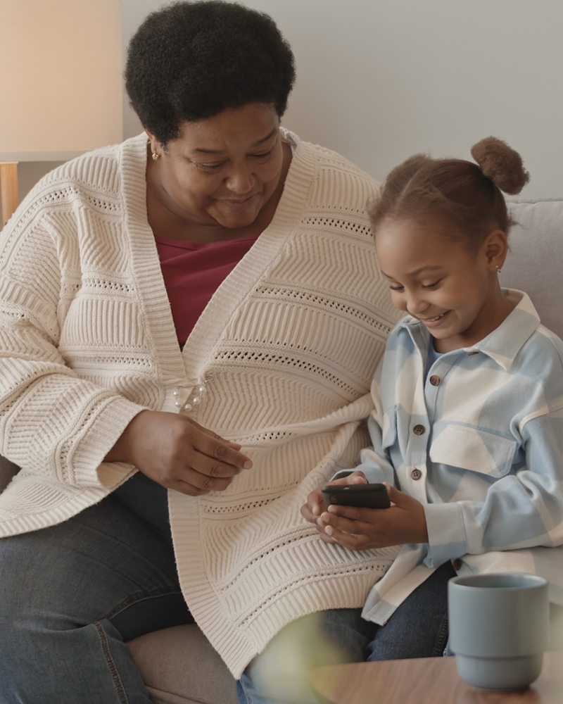 A grandmother and her granddaughter smiling at a phone together on the couch